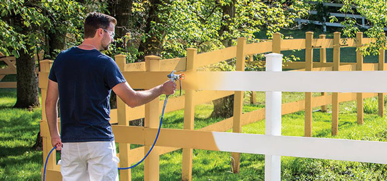 goggled man spray painting white fence yellow